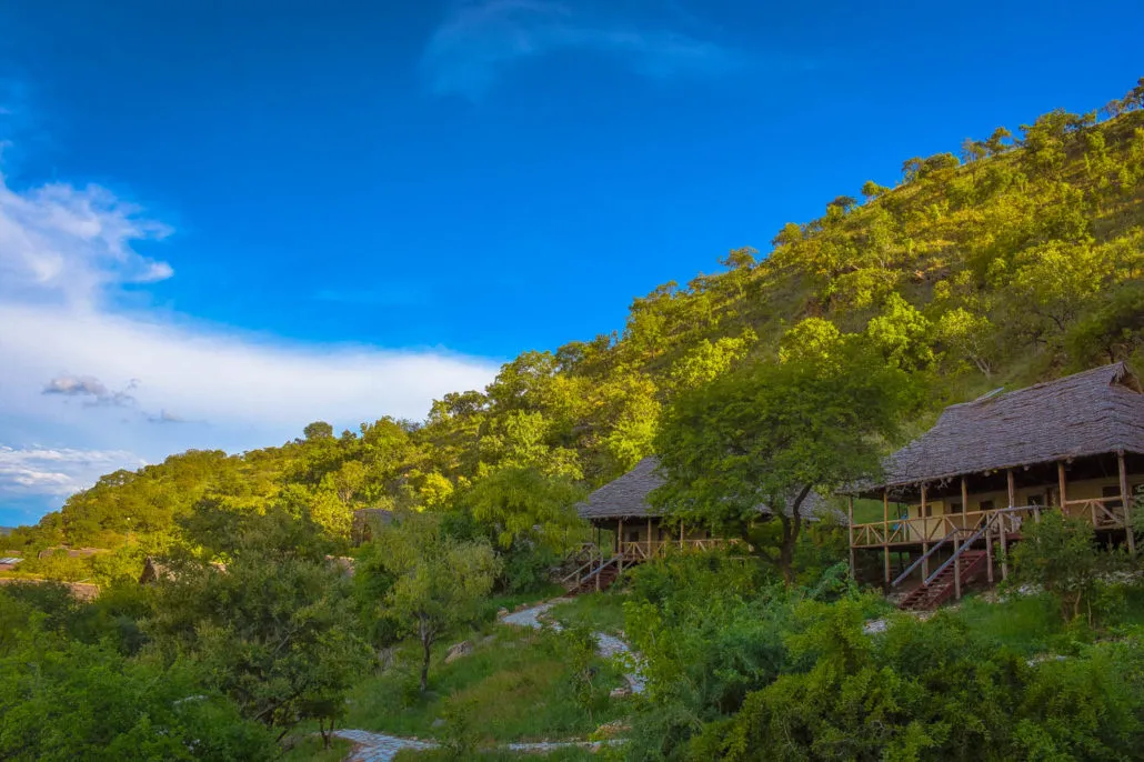 Zelte mit Strohdach am bewaldeten Hang, Sangaiwe Tented Lodge